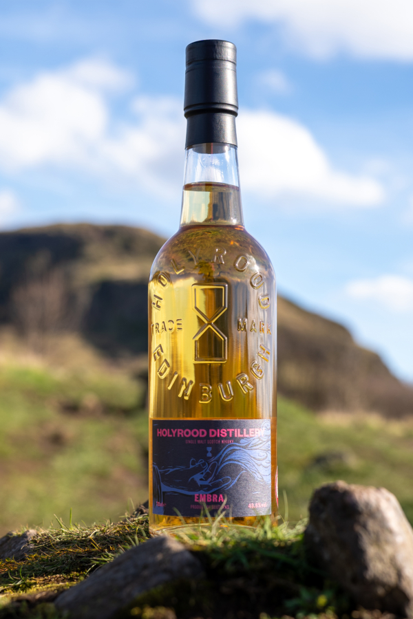 A bottle of Embra single malt Scotch whisky in fornt of Arthur's Seat hill, Edinburgh